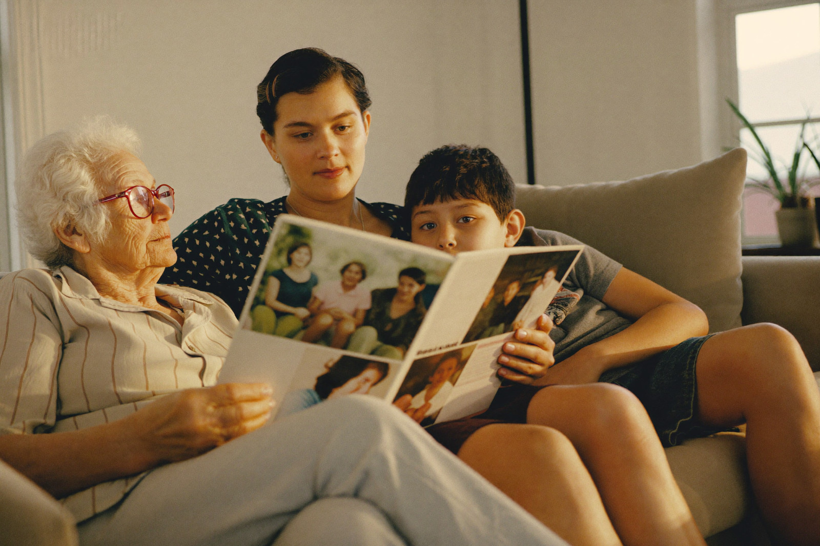 A grandmother, her daughter and her grandson look through a family photo album on the sofa