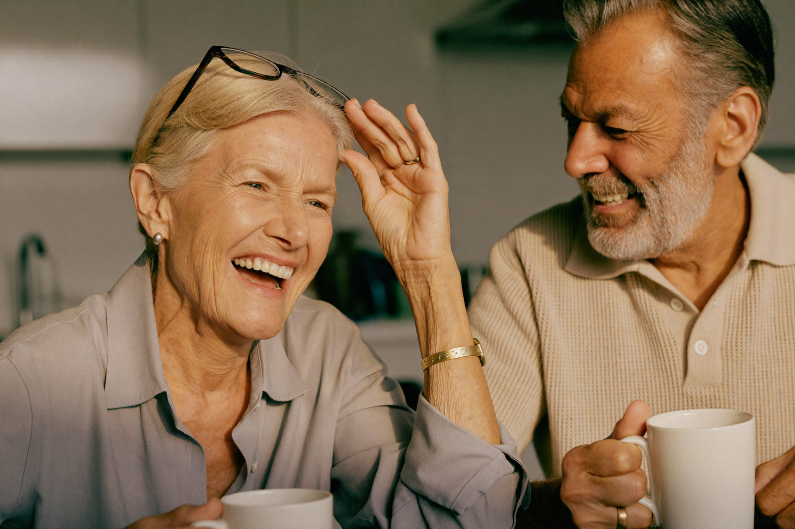 A woman laughs as she finds her reading glasses on her head while her husband smiles