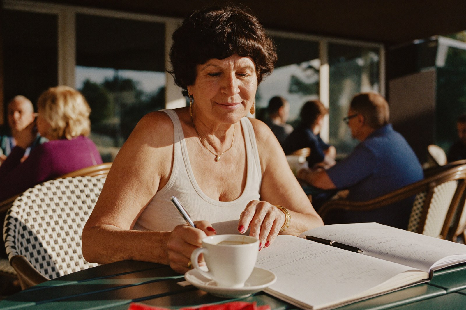 A woman writes in her planner over coffee at a sunny outdoor cafe table