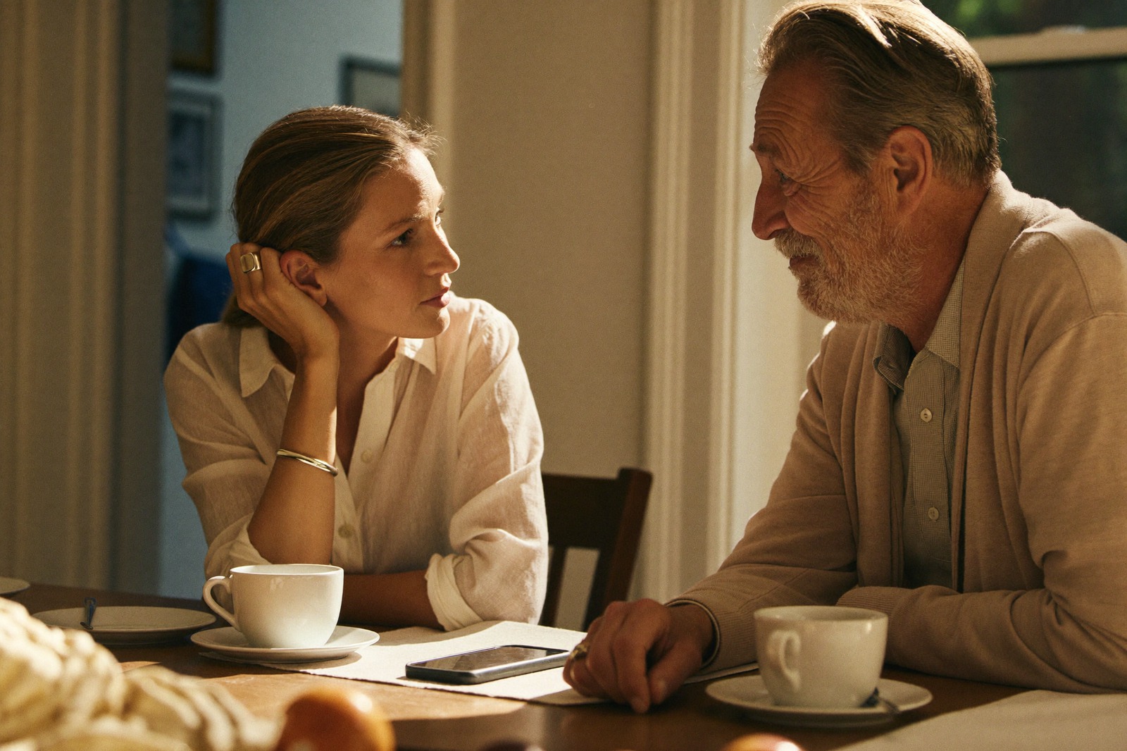 A daughter listens closely as her father talks over coffee at the kitchen table