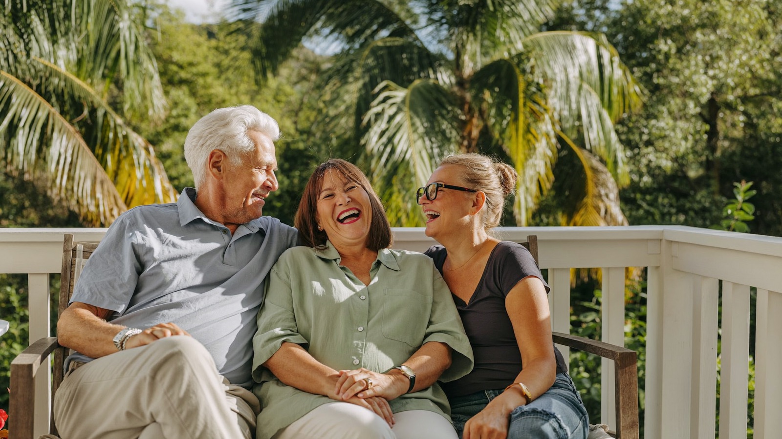 A senior couple laughing with their adult daughter on a bright Florida porch