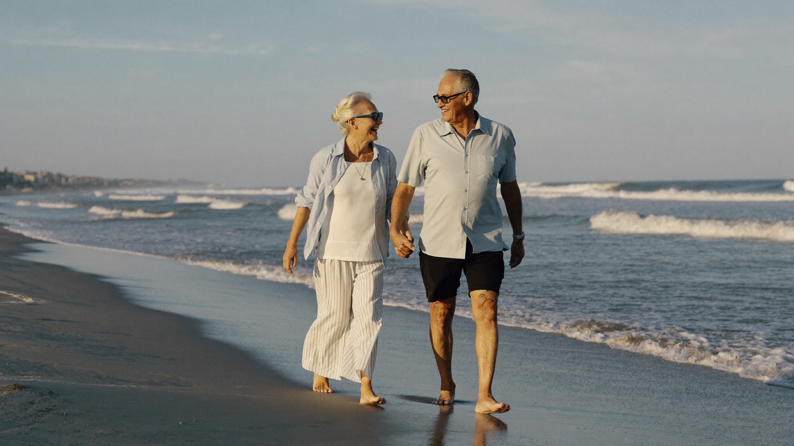 An active senior couple walks hand in hand on a Florida beach at golden hour