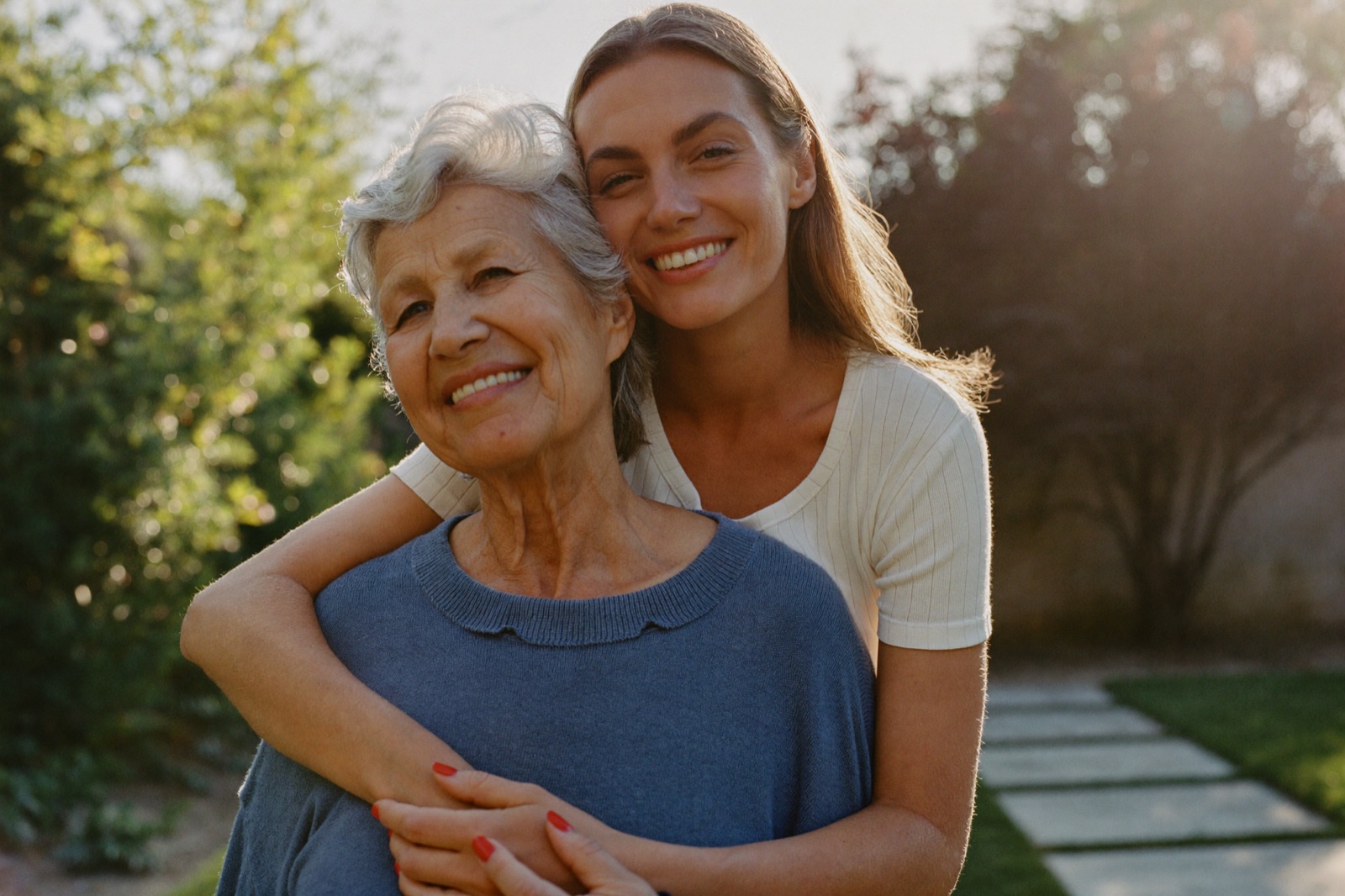 An adult daughter embraces her mother in a garden at golden hour