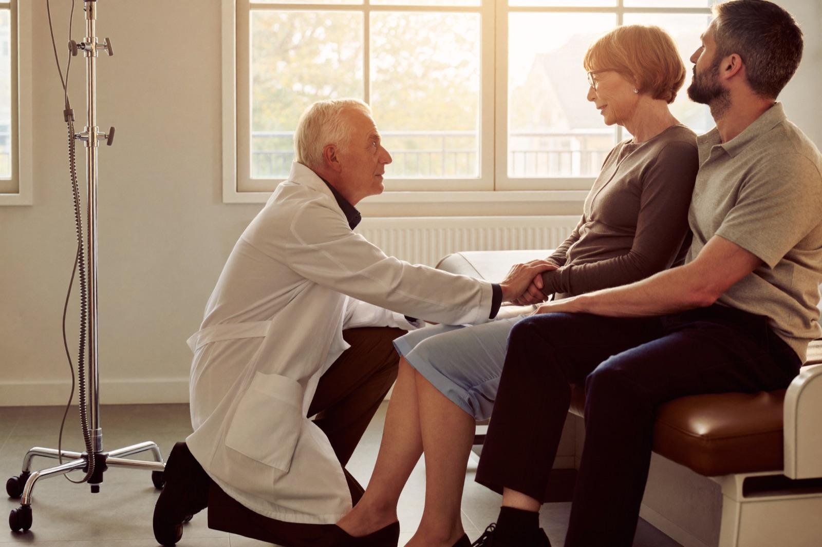 A neurologist sits knee to knee with a patient and her husband, listening