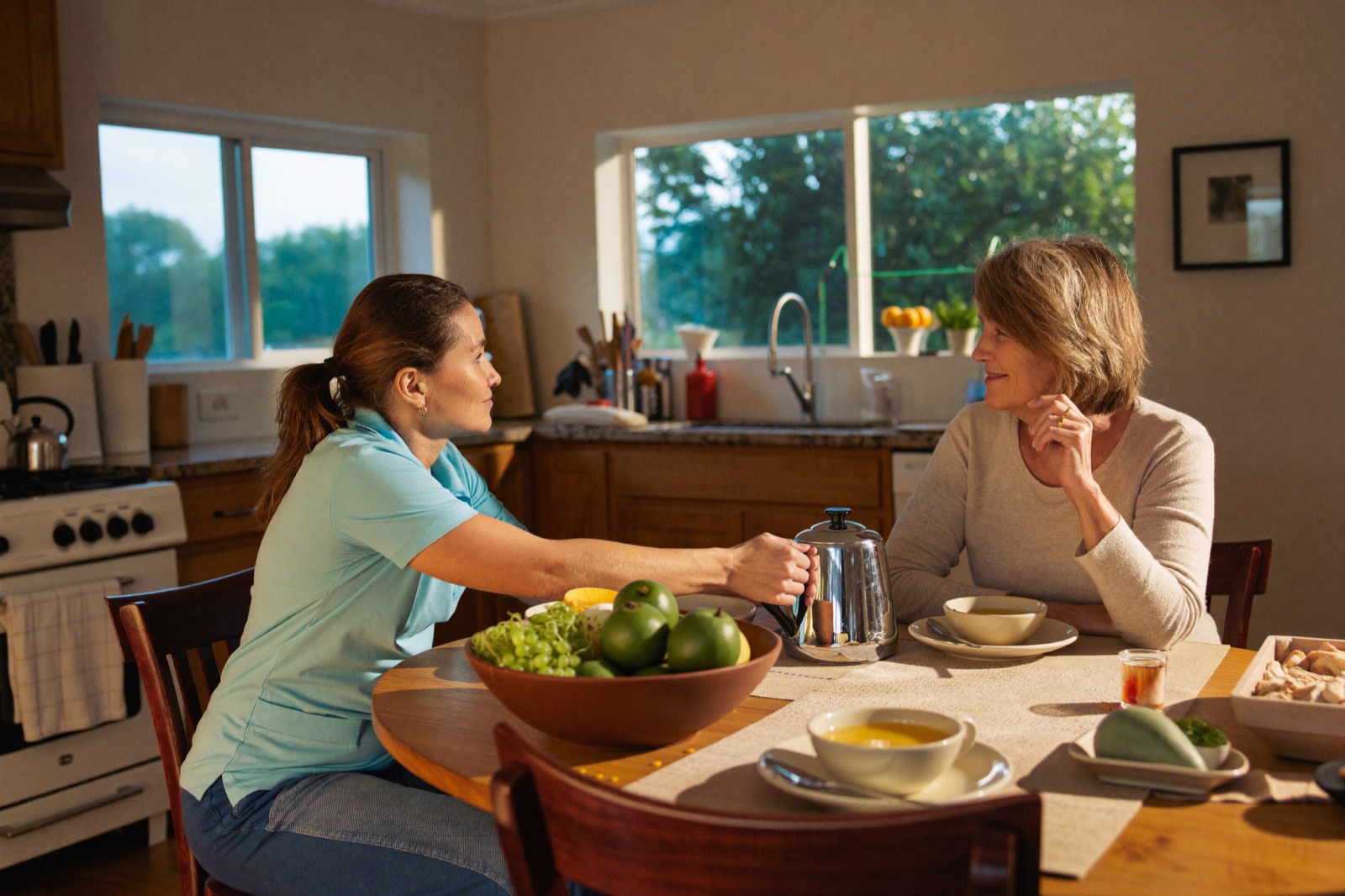 A caregiver shares tea and conversation with a senior woman at home